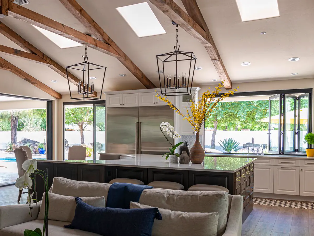 An open plan kitchen with a large island under vaulted beams, opening onto a pool.