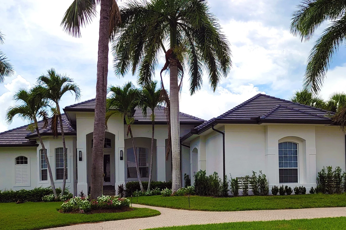 The front of a white stucco Florida home with a dark tile roof, framed by royal palms above a paver walkway.