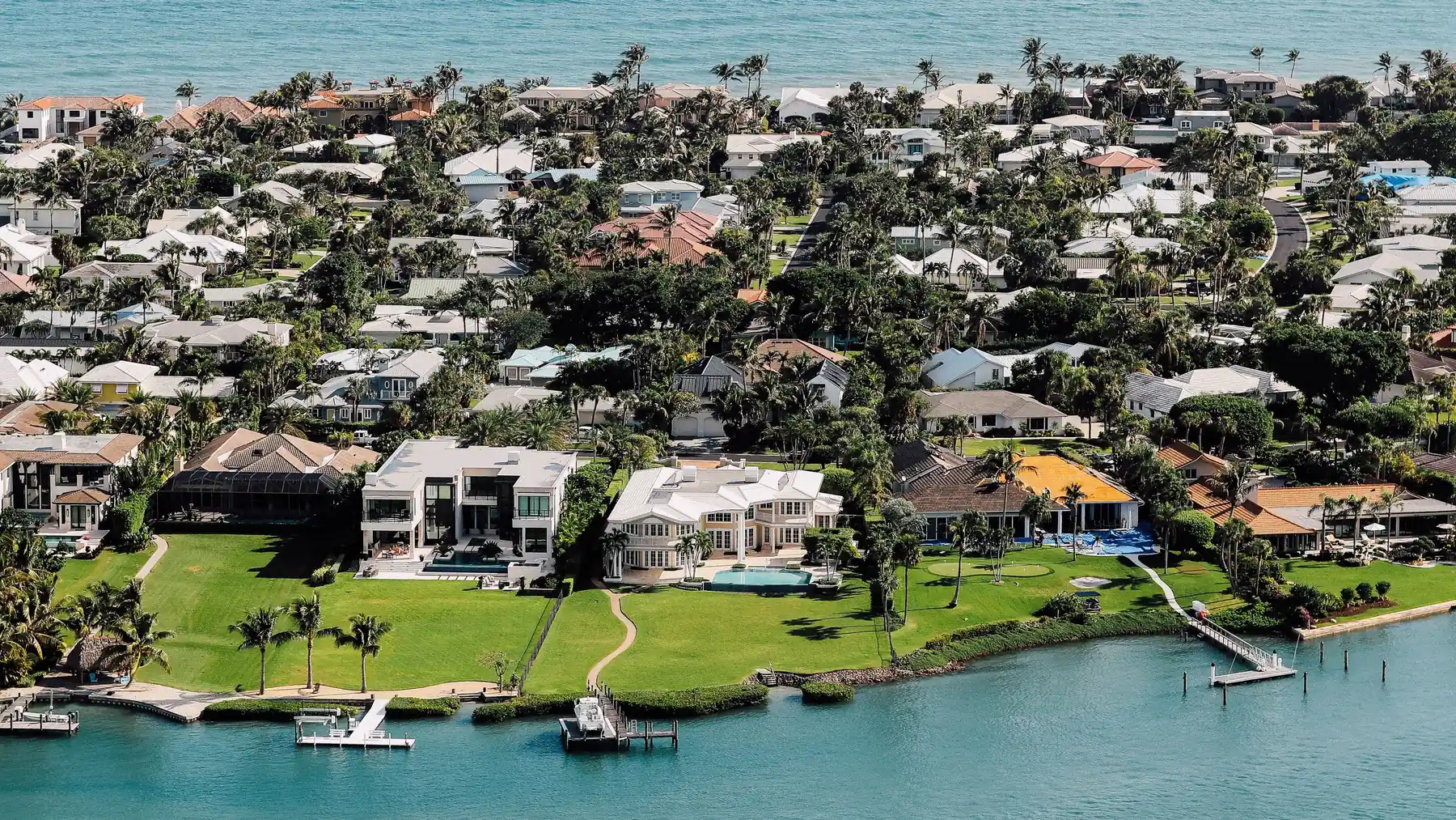 A Florida barrier island seen from the air, with rows of homes, pools and palms between the Gulf and the bay.