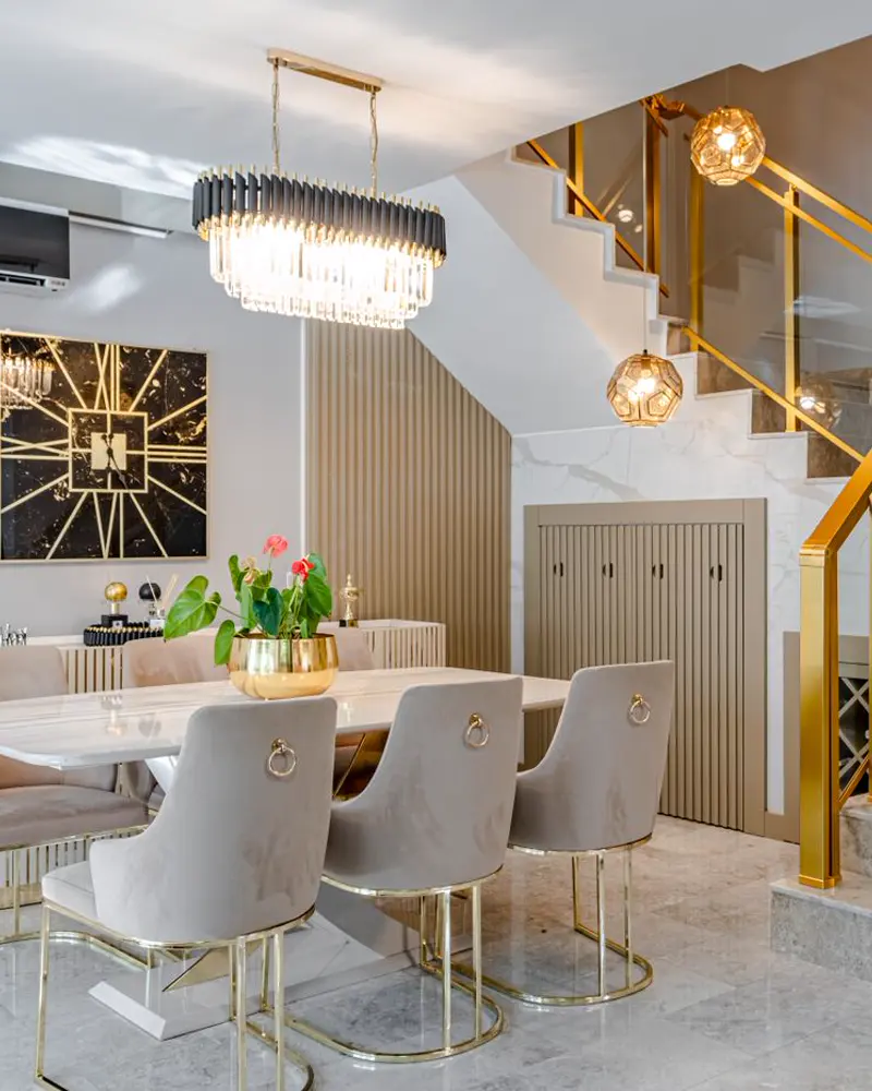 A dining room with a marble table, upholstered chairs and a statement chandelier.