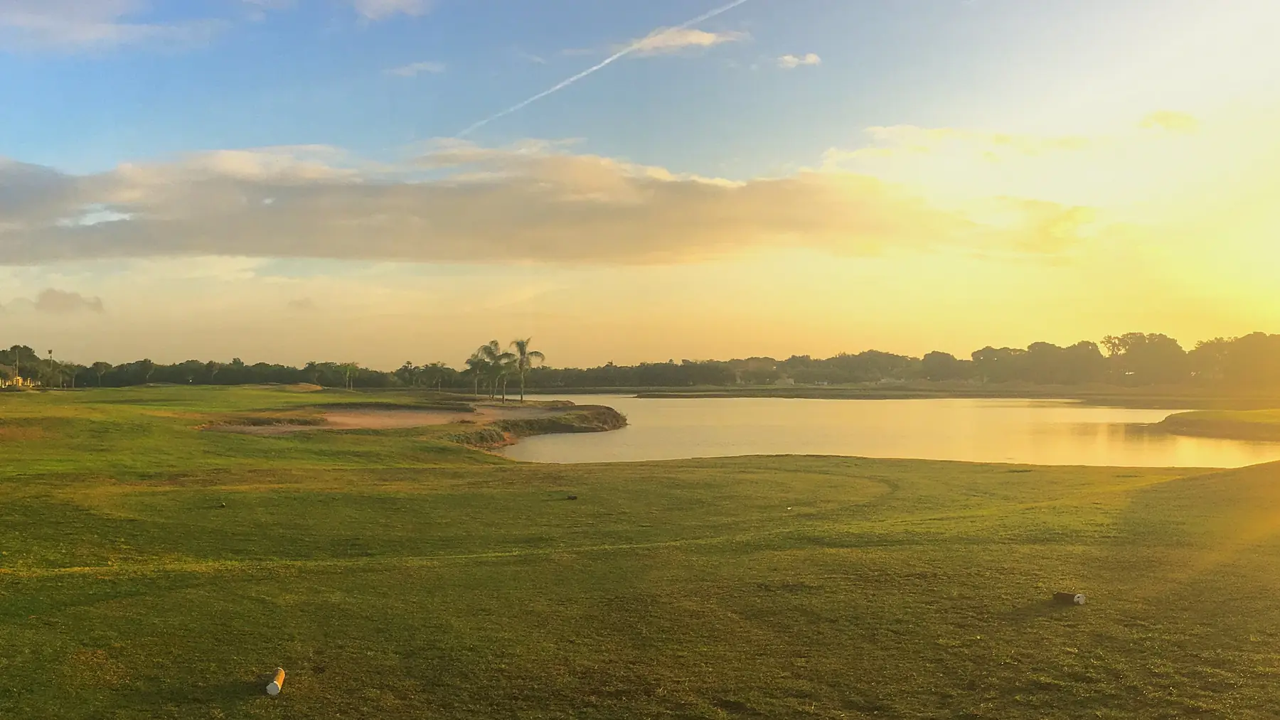 A golf course fairway and water at sunrise.